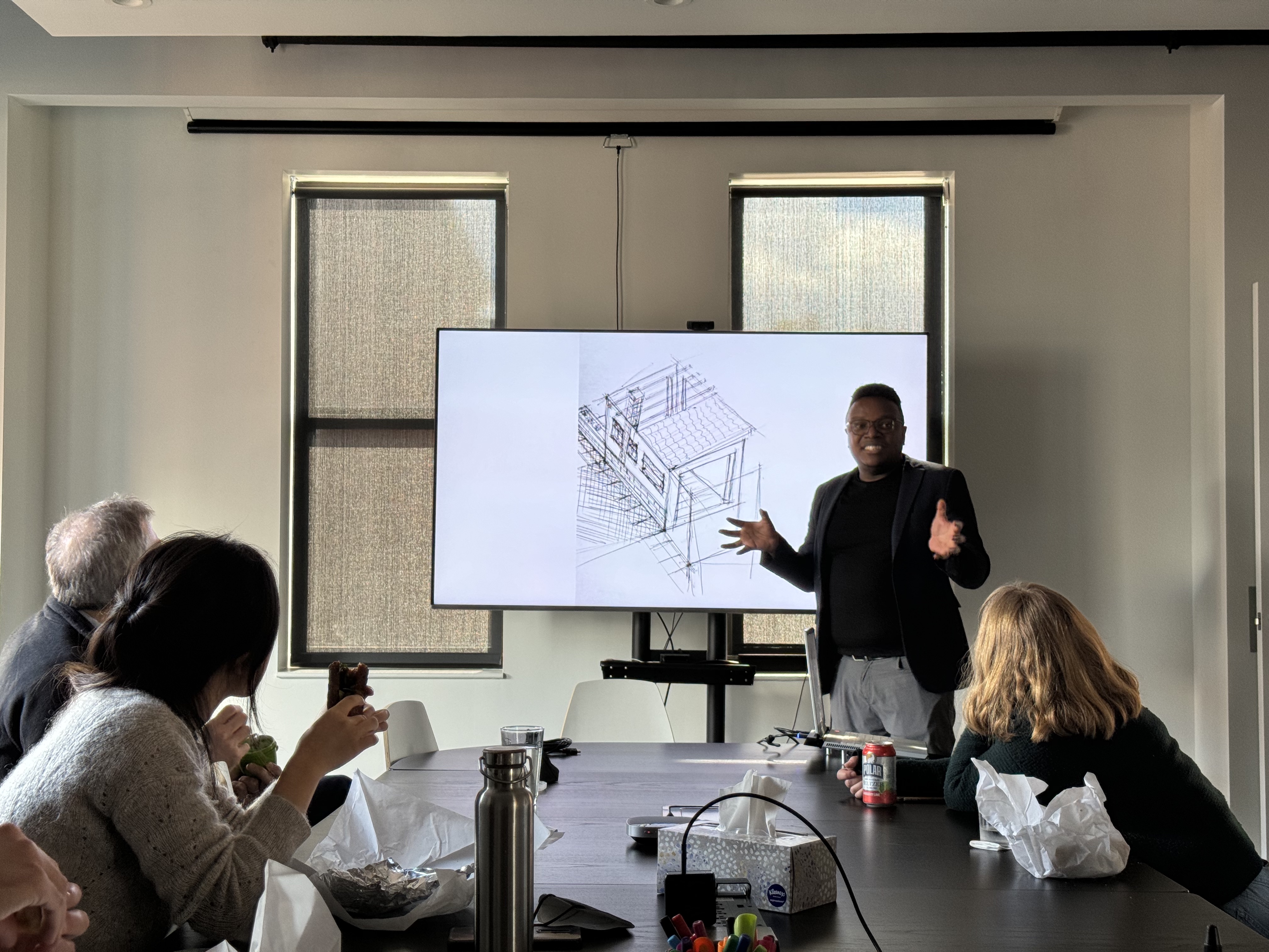 Geoffrey stands at the head of a table full of Fathom employees. He is presenting a screen with an architecture sketch.