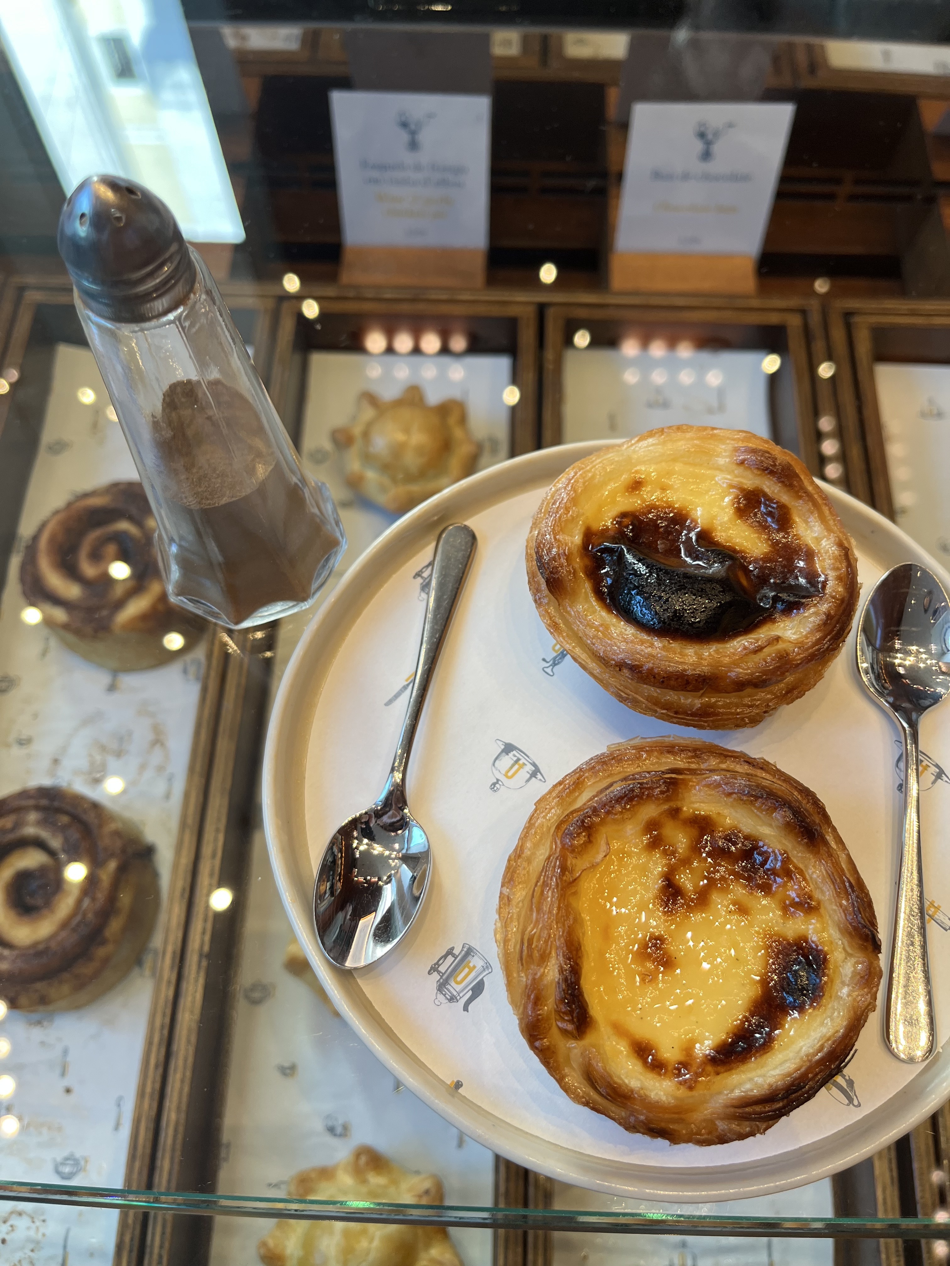 Two pastéis de nata delicately arranged on a plate with a spoon on either side of the pastries.